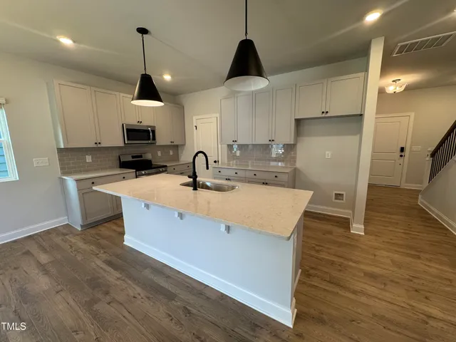 a kitchen with stainless steel appliances a sink a stove a refrigerator a center island and cabinets