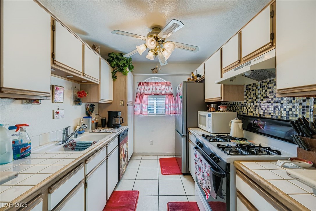 6800 West Elm Creek Drive, Unit 103 Las Vegas, NV 89108 - Photo 11 of 22 Kitchen featuring tile countertops, white appliances, light tile patterned flooring, white cabinetry, and under cabinet range hood