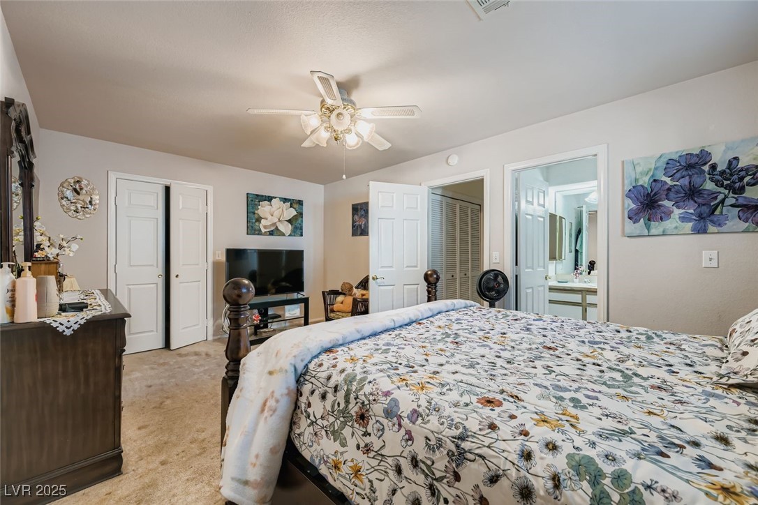 6800 West Elm Creek Drive, Unit 103 Las Vegas, NV 89108 - Photo 15 of 22 Bedroom with two closets, light colored carpet, a ceiling fan, and ensuite bath