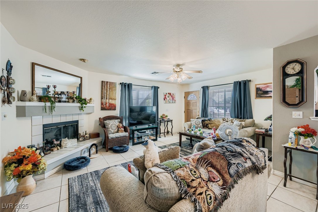 6800 West Elm Creek Drive, Unit 103 Las Vegas, NV 89108 - Photo 6 of 22 Living room featuring a tiled fireplace, light tile patterned flooring, a ceiling fan, and a textured ceiling