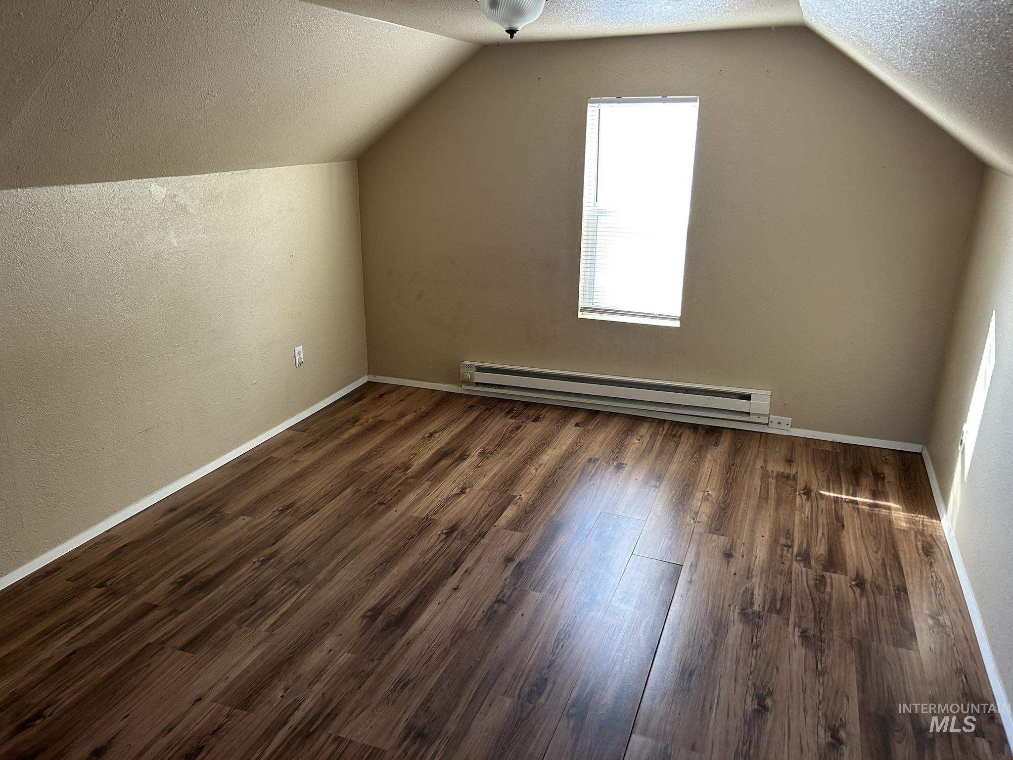 1413 7th Avenue Lewiston, ID 83501 - Photo 10 of 15 Additional living space with a textured ceiling, a textured wall, vaulted ceiling, baseboard heating, and dark wood-type flooring