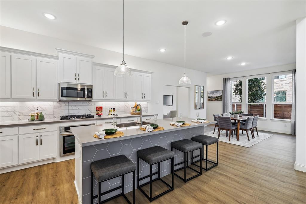 1604 Casting Ridge Mesquite, TX 75181 - Photo 13 of 38 Contemporary open-concept kitchen and dining area featuring white cabinetry, stainless steel appliances, a kitchen island with hexagonal tile detailing, and wood-finish flooring throughout