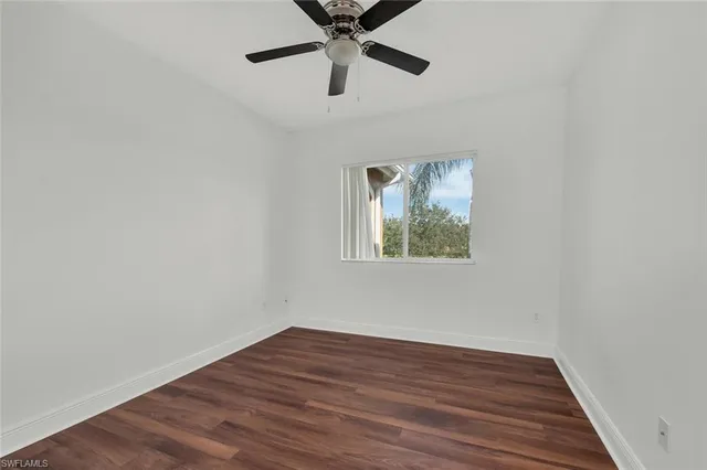 a view of an empty room with wooden floor and a ceiling fan