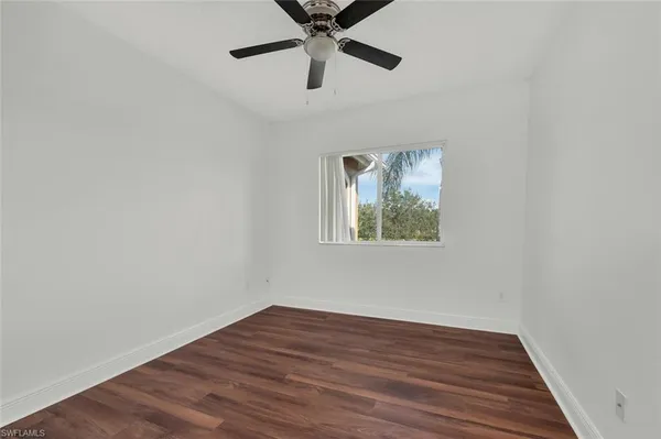 a view of an empty room with wooden floor and a ceiling fan