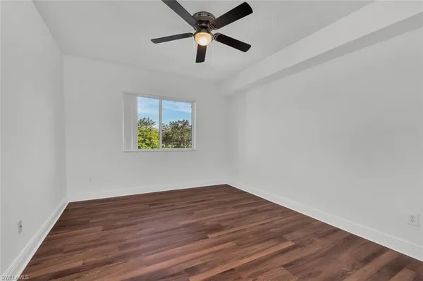 an empty room with wooden floor ceiling fan and windows