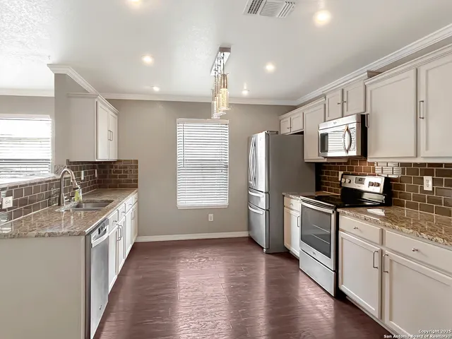 a kitchen with stainless steel appliances granite countertop a refrigerator a stove a sink and white cabinets with wooden floor