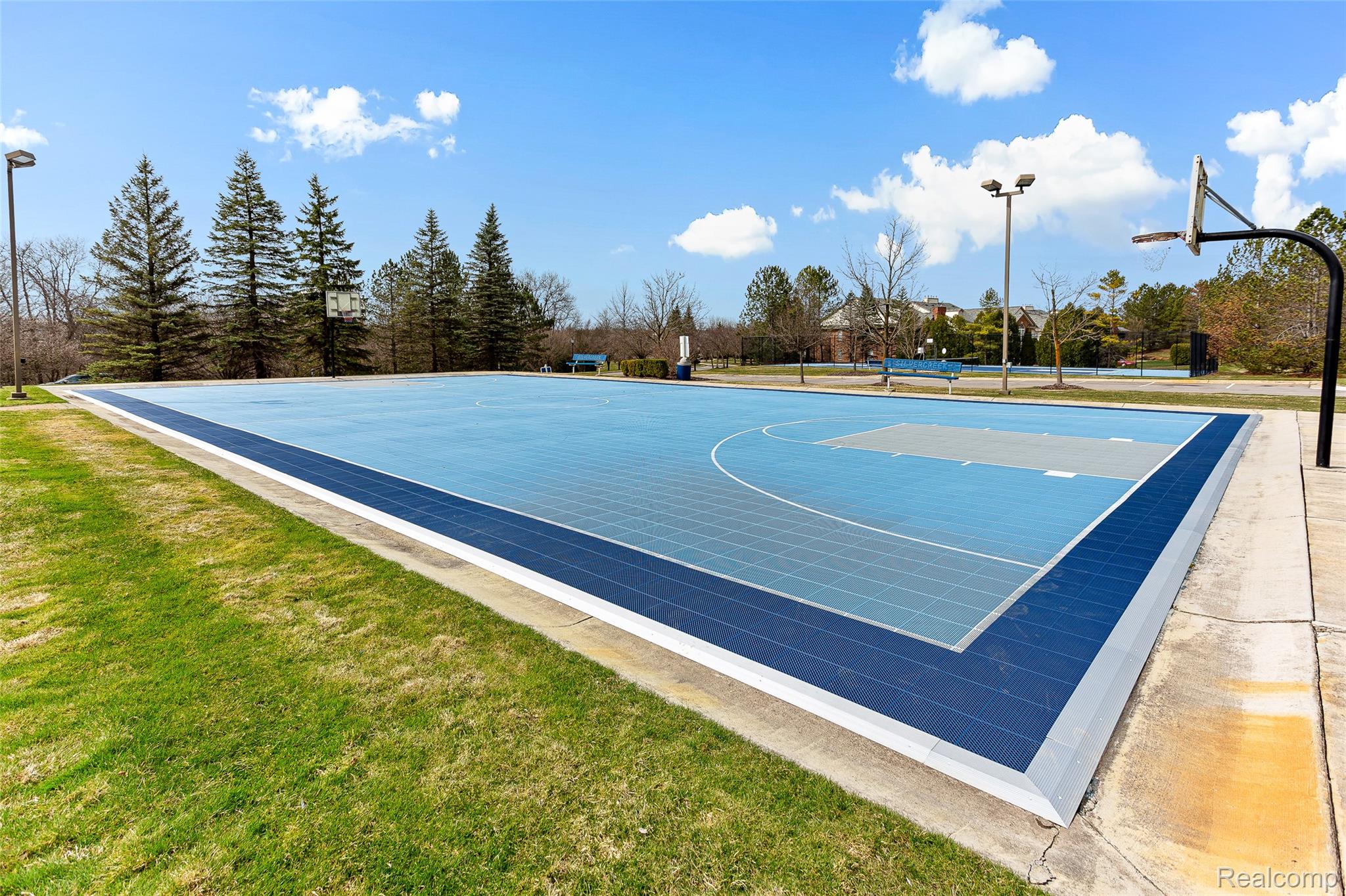 3553 Oakmonte Boulevard Rochester, MI 48306 - Photo 41 of 42 Outdoor basketball court with blue and gray playing surfaces, surrounded by green grass and concrete pathways