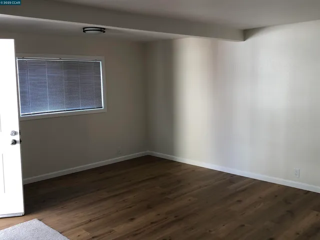 a view of an empty room with wooden floor and a window