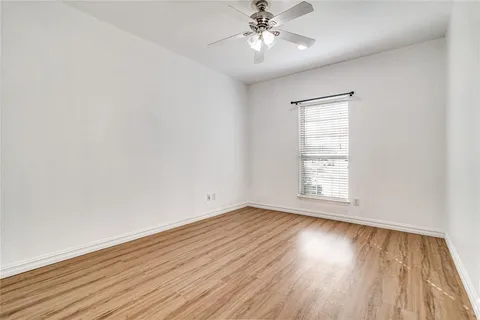 an empty room with wooden floor chandelier fan and windows