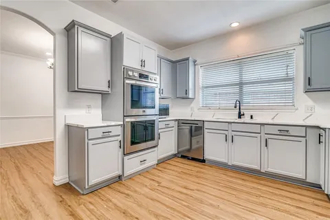 a kitchen with stainless steel appliances granite countertop a stove a sink dishwasher a refrigerator and white cabinets with wooden floor