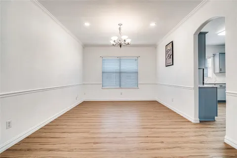 an empty room with wooden floor chandelier and windows