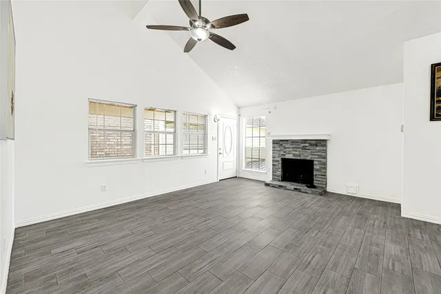 an empty room with wooden floor fireplace and windows