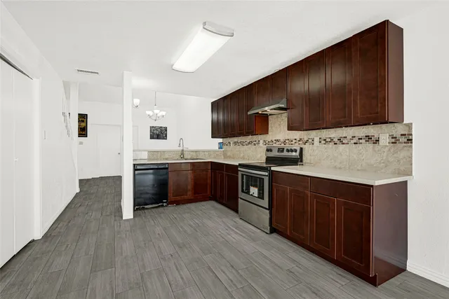 a kitchen with stainless steel appliances kitchen island granite countertop wooden cabinets a sink a stove a refrigerator and island with wooden floor