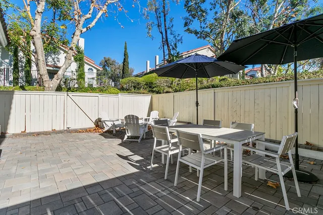 a view of patio with chairs and table under an umbrella with barbeque grill and wooden fence