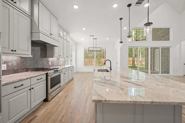 a kitchen with stainless steel appliances granite countertop a stove a sink and white cabinets with wooden floor