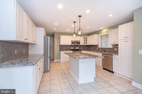 a kitchen with stainless steel appliances granite countertop a stove top oven a sink a refrigerator and white cabinets