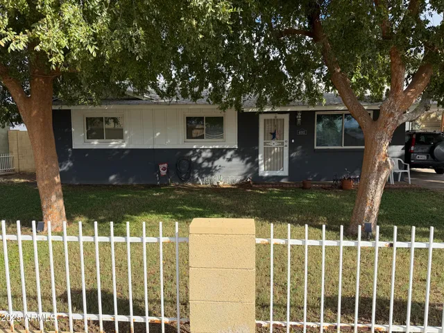 a view of house with wooden fence and a large tree