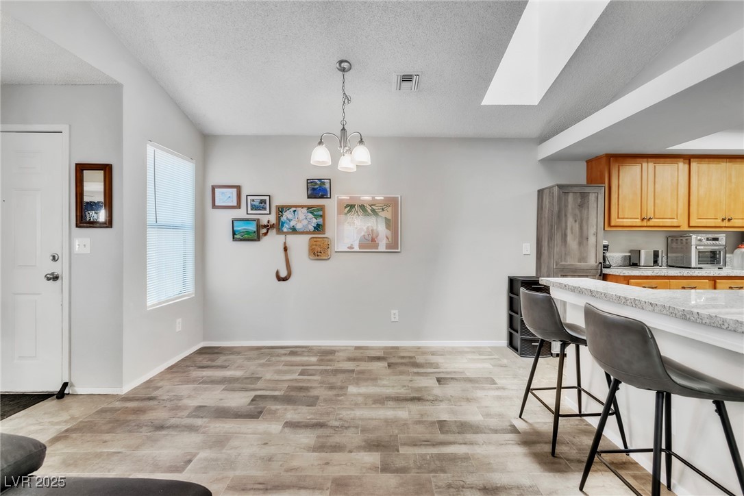 2995 East Sunset Road, Unit 235 Las Vegas, NV 89120 - Photo 3 of 24 Kitchen with a kitchen breakfast bar, a textured ceiling, decorative light fixtures, a skylight, and light wood-style flooring