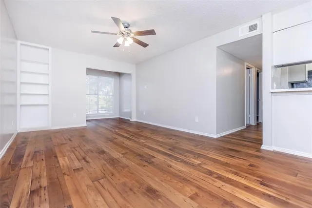 a view of empty room with wooden floor and fan