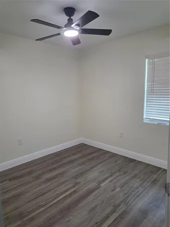 a view of an empty room with wooden floor and a ceiling fan