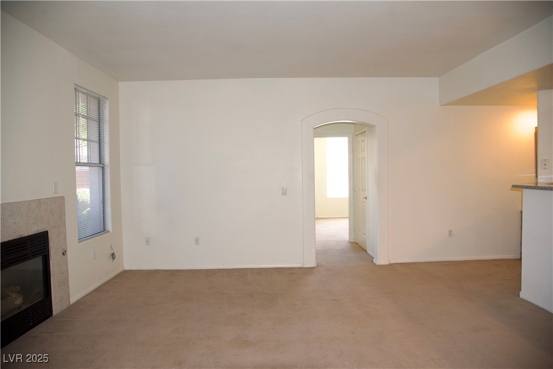 8555 West Russell Road, Unit 1078 Las Vegas, NV 89113 - Photo 16 of 34 Unfurnished living room featuring arched walkways, a tiled fireplace, carpet flooring, and healthy amount of natural light