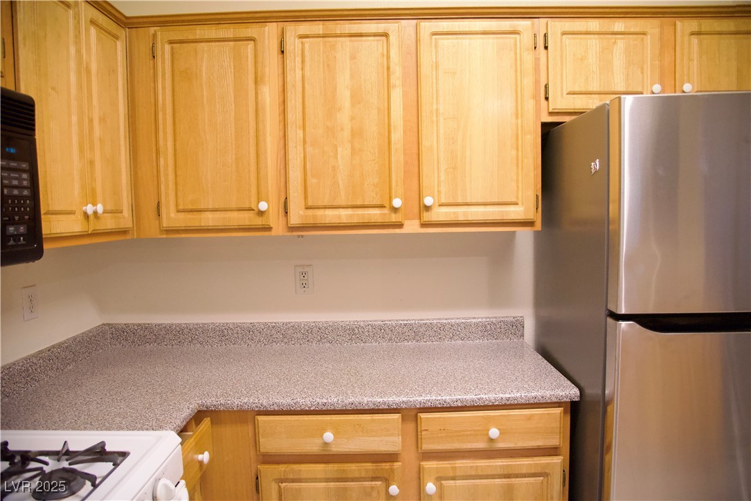 8555 West Russell Road, Unit 1078 Las Vegas, NV 89113 - Photo 17 of 34 Kitchen with freestanding refrigerator, white range with gas stovetop, black microwave, and light stone countertops