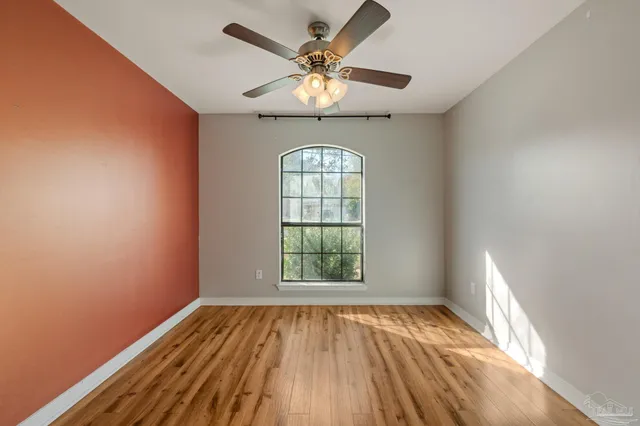 an empty room with wooden floor fan and windows