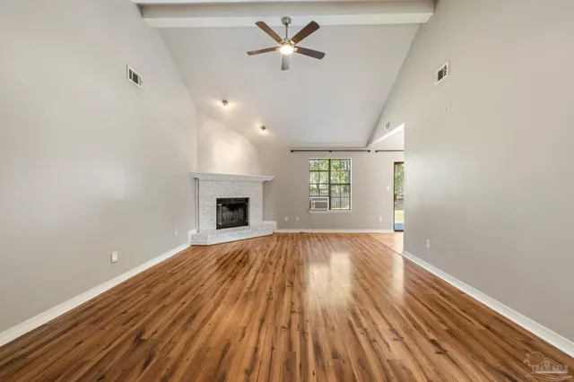 an empty room with wooden floor fireplace and windows