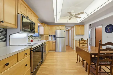 a kitchen with stainless steel appliances granite countertop a refrigerator a oven a sink a dining table and chairs with wooden floor