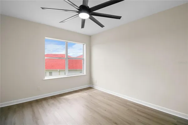 an empty room with wooden floor chandelier fan and windows