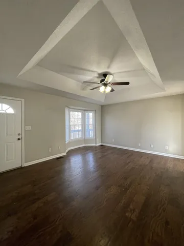 an empty room with wooden floor fan and windows