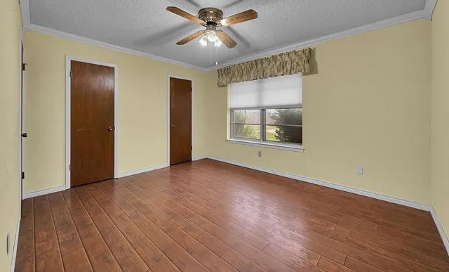 an empty room with wooden floor chandelier fan and windows