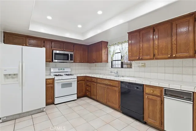 a kitchen with stainless steel appliances granite countertop a stove top oven a sink dishwasher and a refrigerator with wooden cabinets