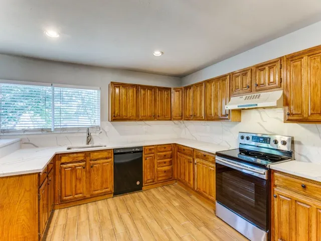 a kitchen with stainless steel appliances granite countertop wooden cabinets a stove top oven a sink and dishwasher with wooden floor