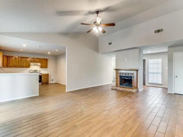a view of an empty room with wooden floor and a kitchen