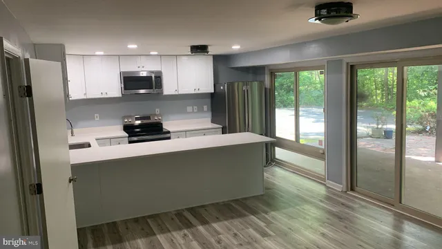 a kitchen with stainless steel appliances granite countertop a refrigerator a sink a stove and white cabinets with wooden floor