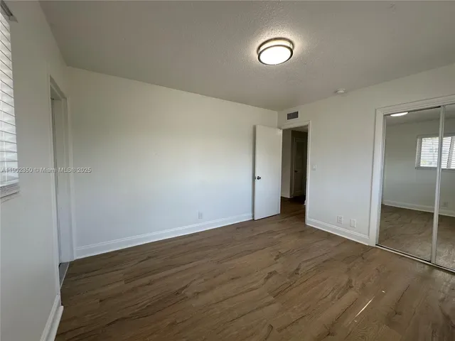 an empty room with wooden floor closet and windows