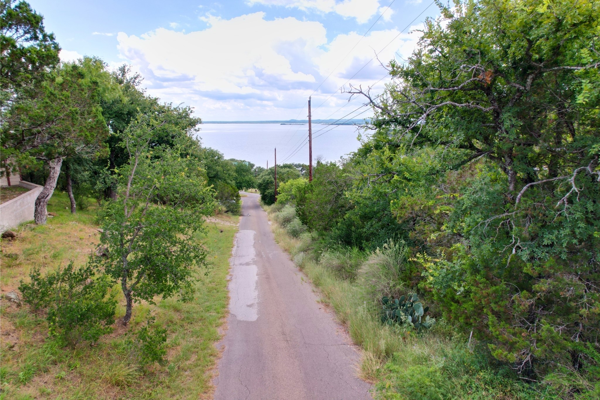 706 Cr138a Road Burnet, TX 78611 - Photo 5 of 18 A tranquil road leads down to the calm, distant lake, surrounded by a lush green landscape.