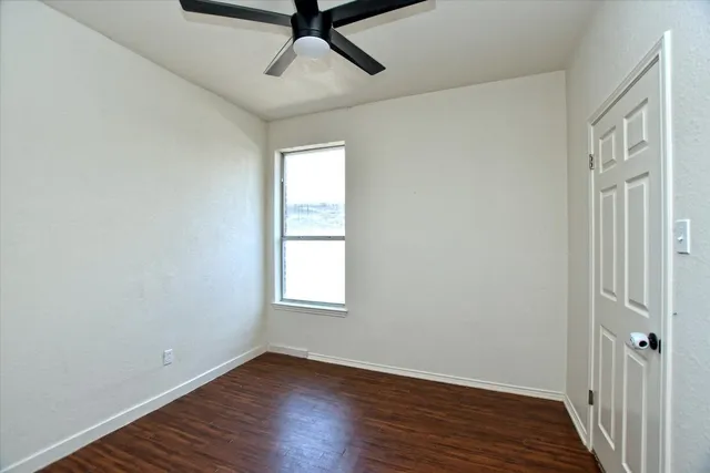 an empty room with wooden floor fan and windows