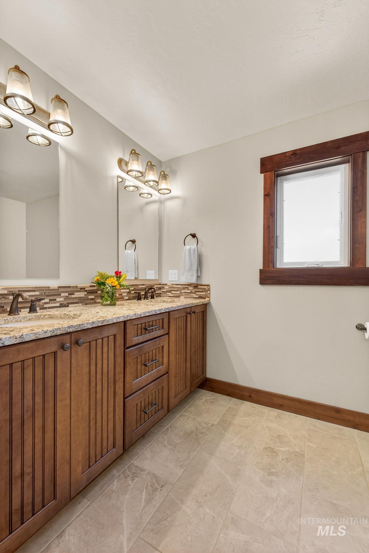 13388 Norwood Road McCall, ID 83638 - Photo 26 of 44 Dual vanity featuring granite countertops, wood-finish cabinetry, and a tile backsplash