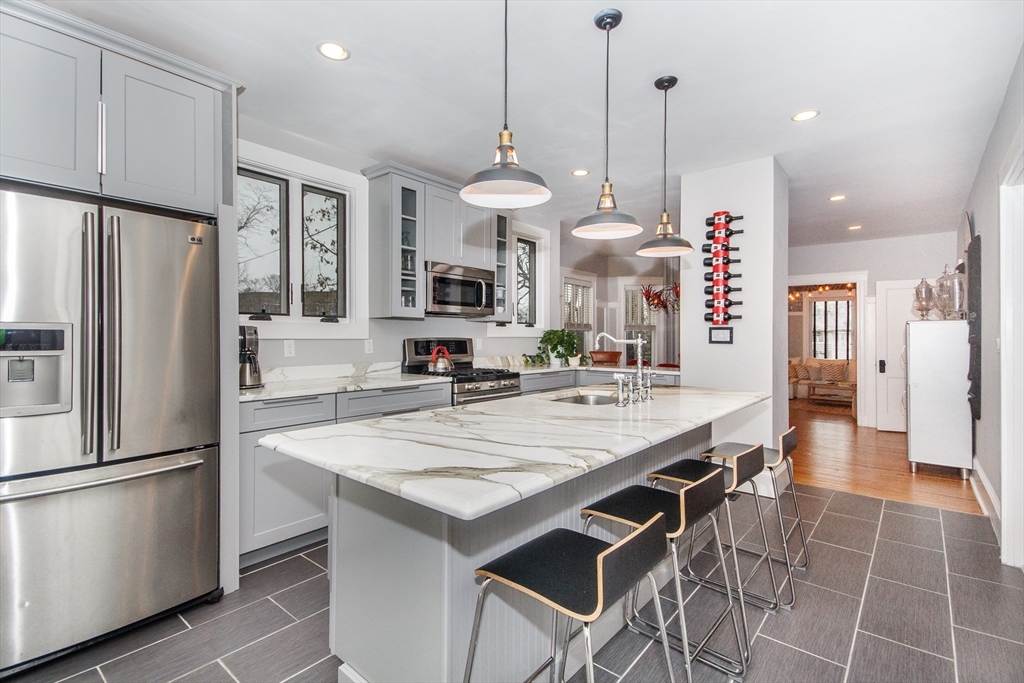 a kitchen with stainless steel appliances granite countertop a refrigerator a sink dishwasher a stove a dining table and chairs with wooden floor