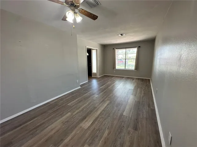 an empty room with wooden floor chandelier fan and windows
