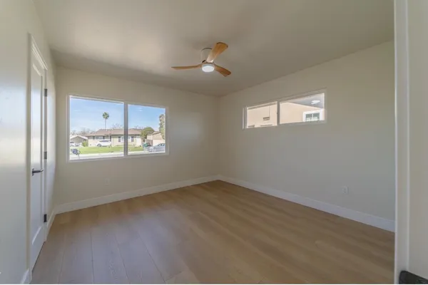 an empty room with wooden floor ceiling fan and windows