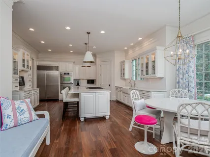 a kitchen with stainless steel appliances kitchen island granite countertop a refrigerator a sink dishwasher a dining table and chairs with wooden floor