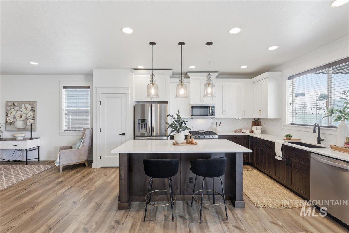 5897 West Riva Capri Street Meridian, ID 83646 - Photo 5 of 50 Open-concept kitchen featuring a large island with seating, stainless steel appliances, white upper cabinetry, dark wood-finish lower cabinetry, and wood-finish flooring