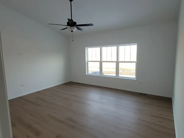 an empty room with wooden floor chandelier fan and windows