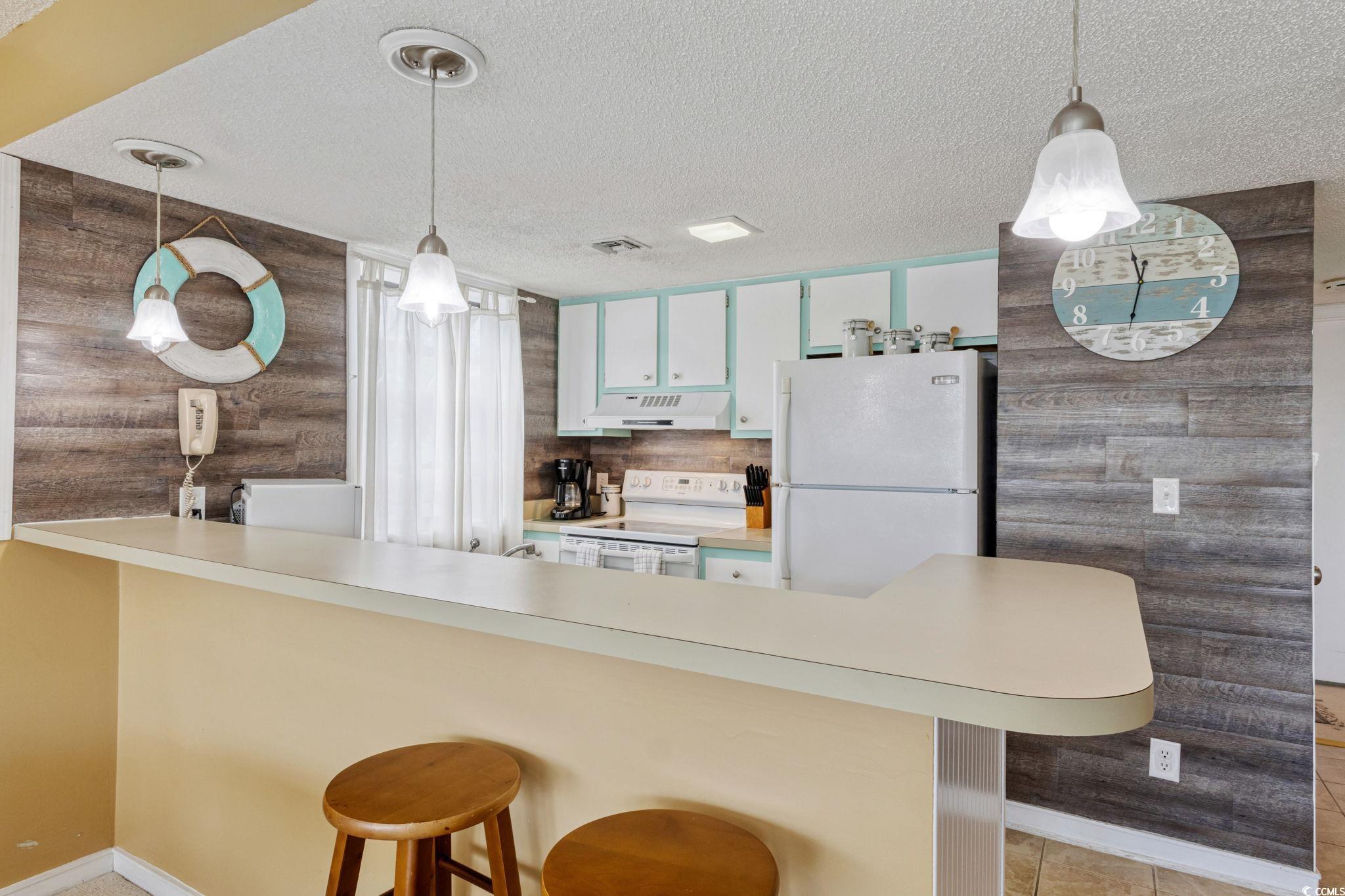 351 Lake Arrowhead Road, Unit 2206 Myrtle Beach, SC 29572 - Photo 7 of 40 Kitchen featuring wooden walls, a breakfast bar area, pendant lighting, white appliances, and light countertops
