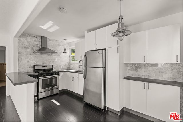 a kitchen with stainless steel appliances granite countertop a refrigerator a stove a sink dishwasher a oven with white cabinets and wooden floor