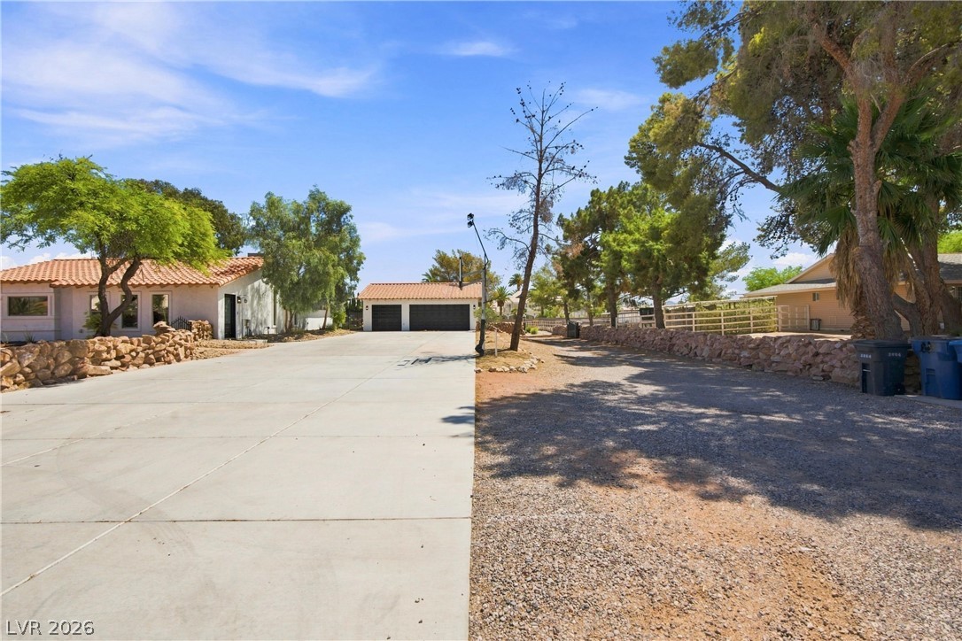 7744 Rancho Destino Road Las Vegas, NV 89123 - Photo 3 of 48 Mature trees frame a wide concrete driveway leading toward a detached multi-car garage.