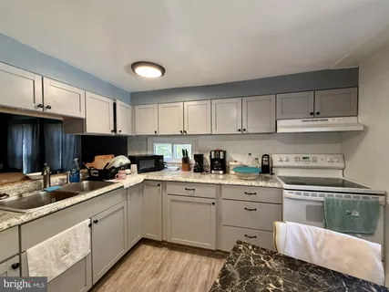 a kitchen with a sink dishwasher a stove and white cabinets with wooden floor